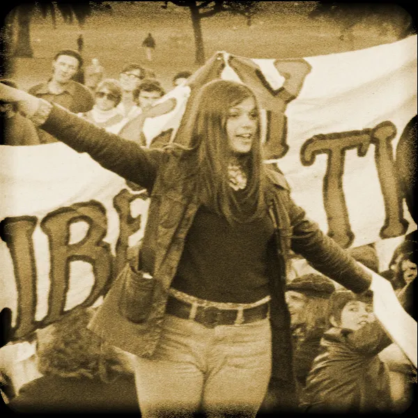 A protester at a 1970s gay liberation march, arms outstretched in front of banners